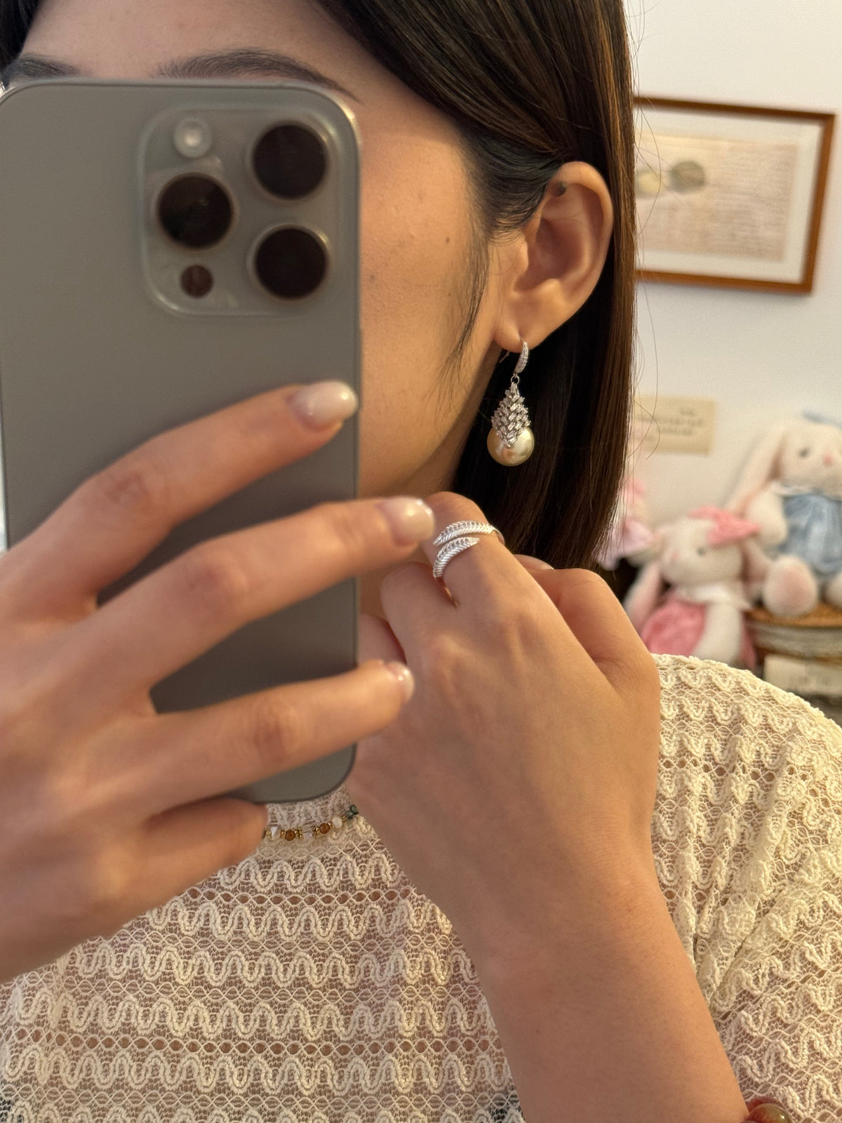 Woman wearing pearl drop earrings and a silver crystal ring in a mirror selfie