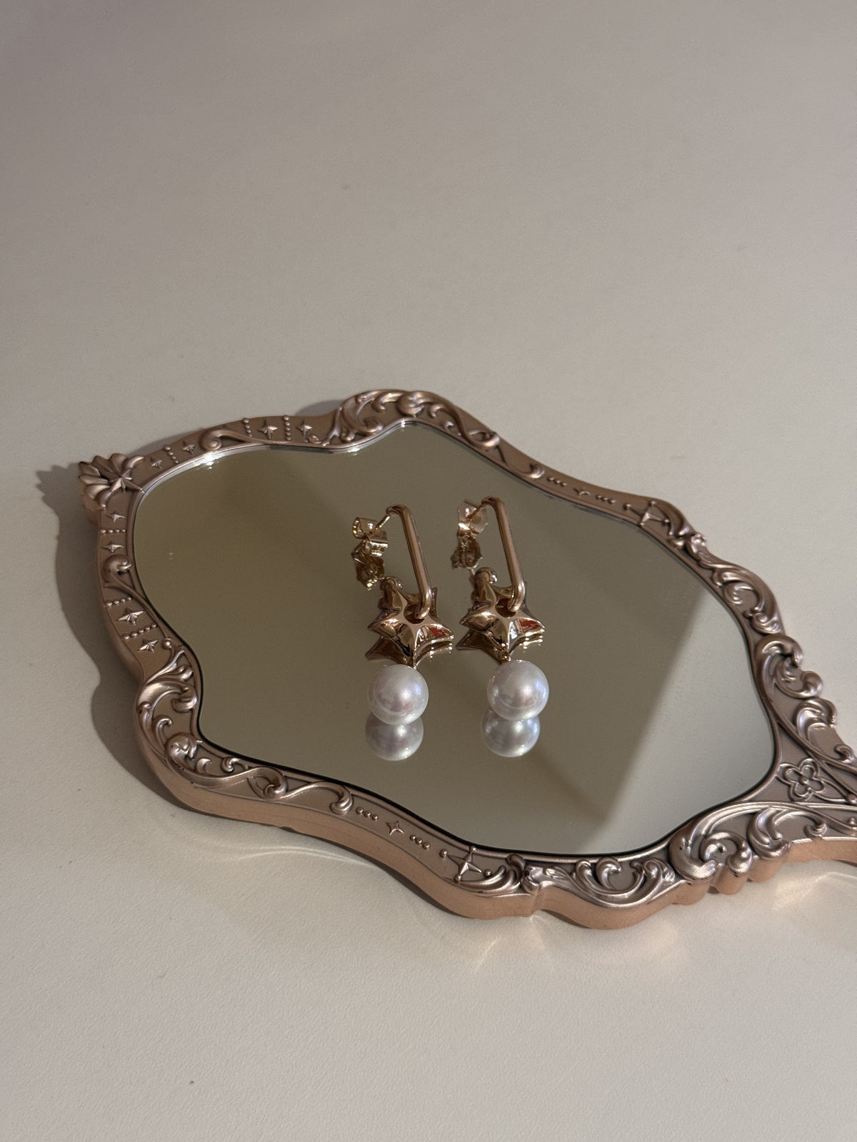 A pair of gold-tone star earrings with dangling white pearls displayed on a mirrored tray.