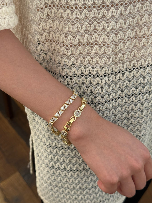 Woman's wrist in cream lace sleeve wearing two gold-tone bracelets with clear crystal accents.