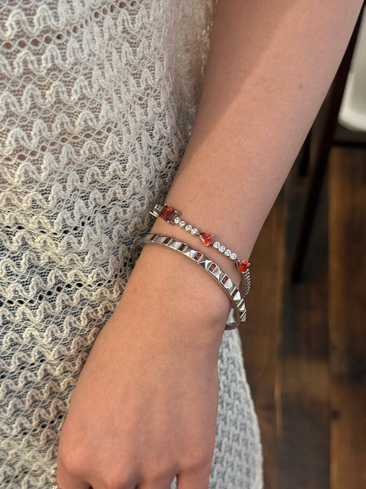 Two silver bracelets on wrist: one red crystal chain, one pyramid stud bangle, lace background.