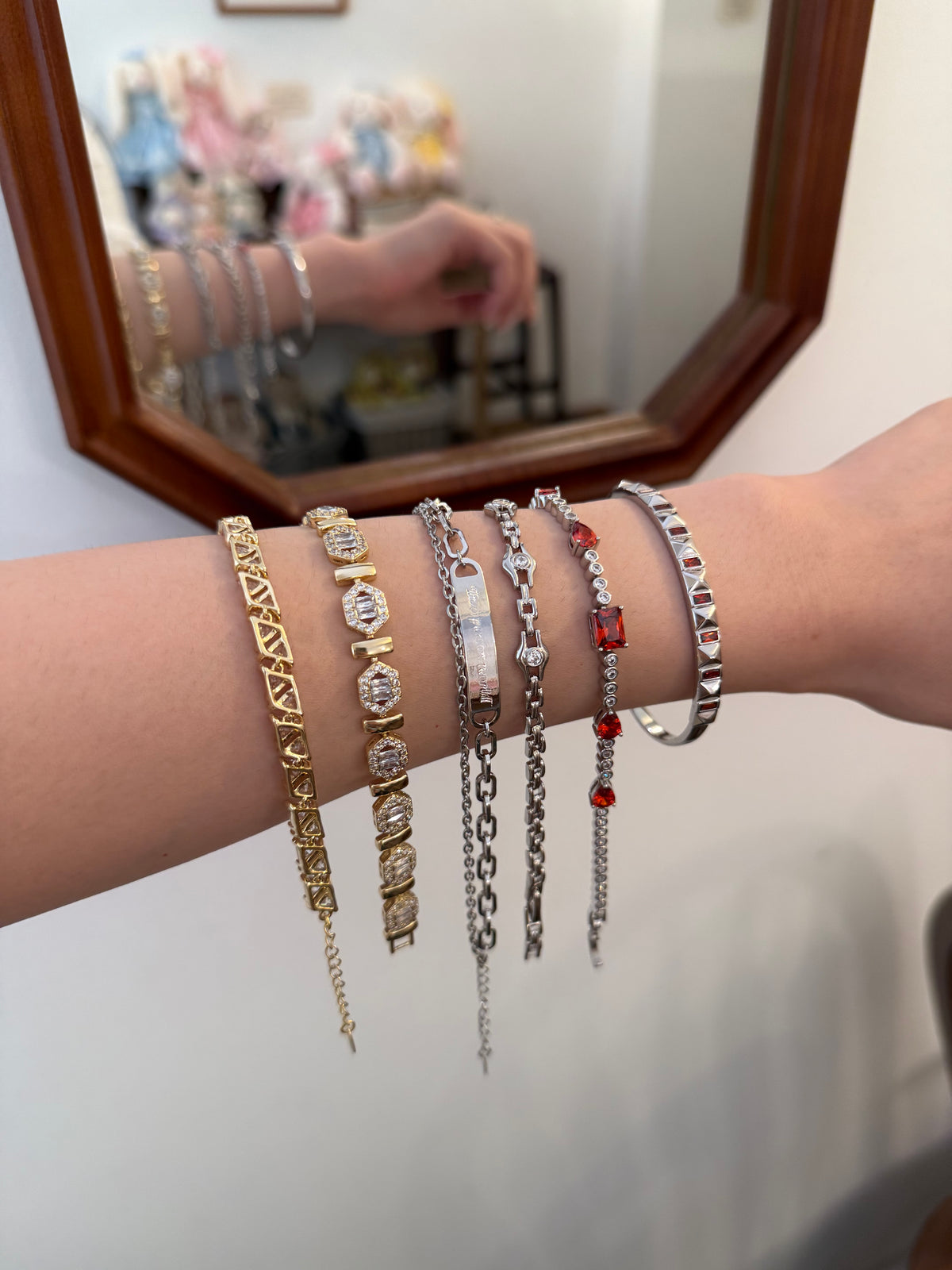 Woman's arm wearing stacked gold and silver chain bracelets with crystals and red accents