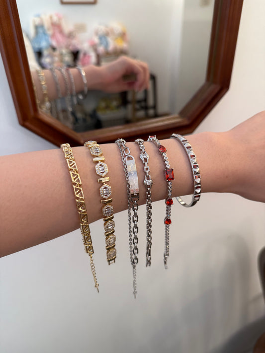 Woman's arm wearing stacked gold and silver chain bracelets with crystals and red accents