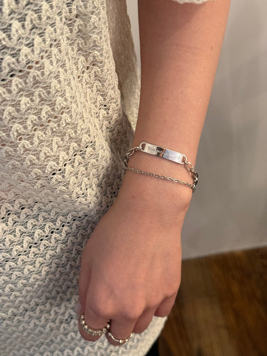 Silver layered chain bracelet with rectangular bar tag and fine chain on wrist.