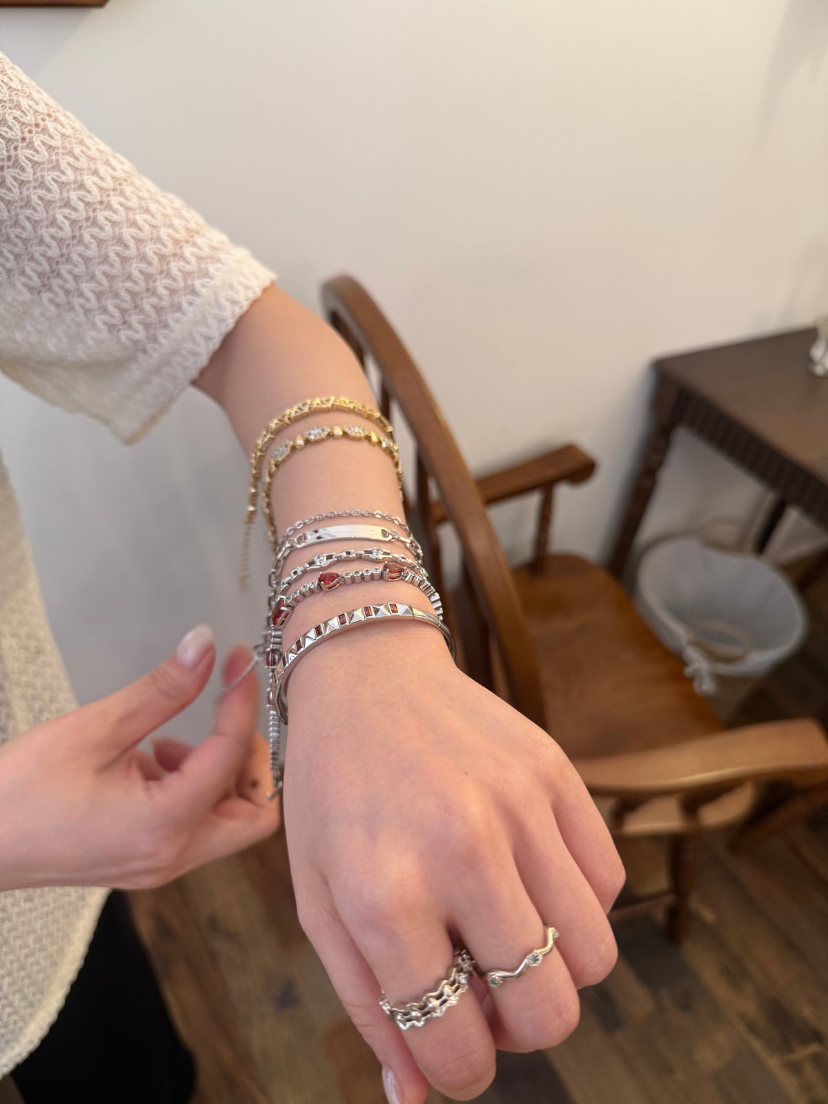 Woman's wrist stacked with gold and silver chain bracelets and rings in a fashion jewelry product photo