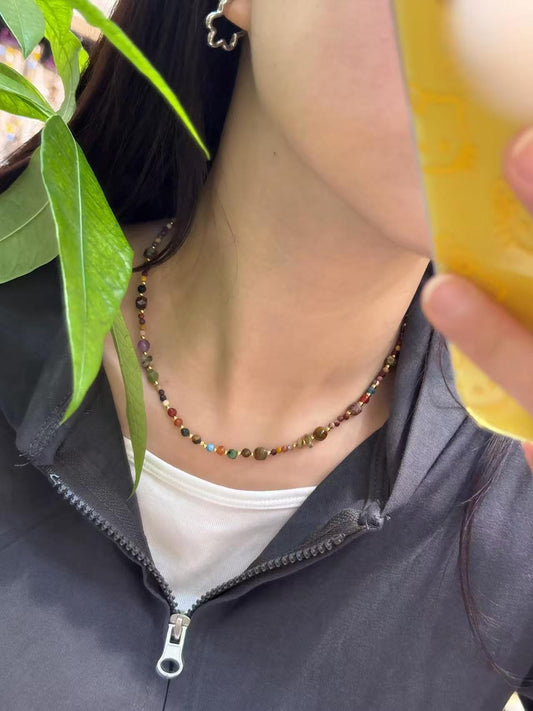 Close-up of a multicolored beaded gemstone necklace worn on a neck, with green leaves on the left.