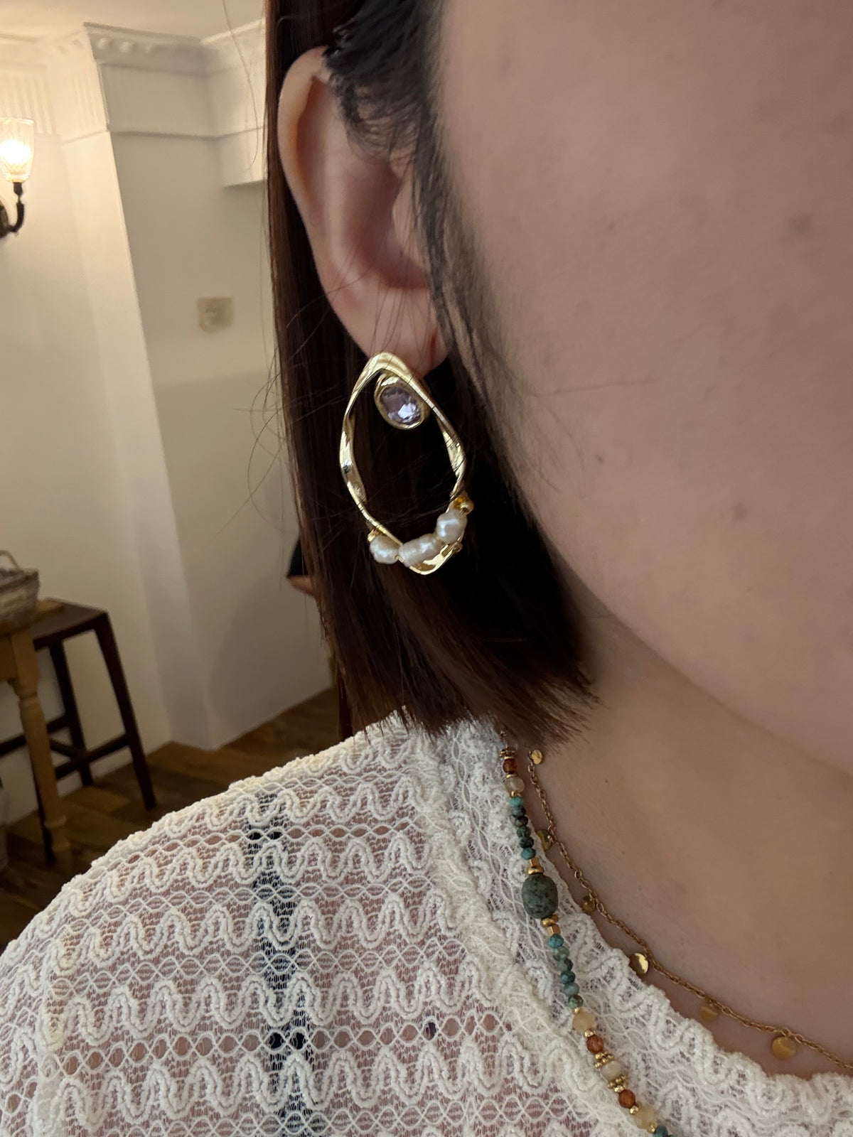 Gold-tone twisted open-loop earring with a purple crystal and small pearl accents, worn on model's ear.