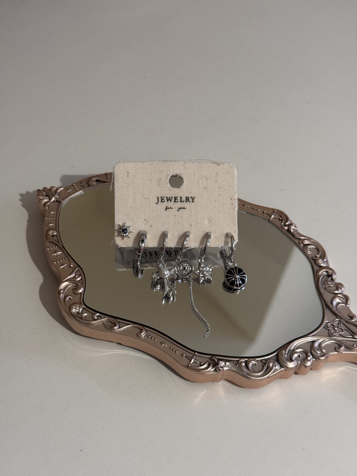 A set of silver-tone earrings with assorted charms on a card.