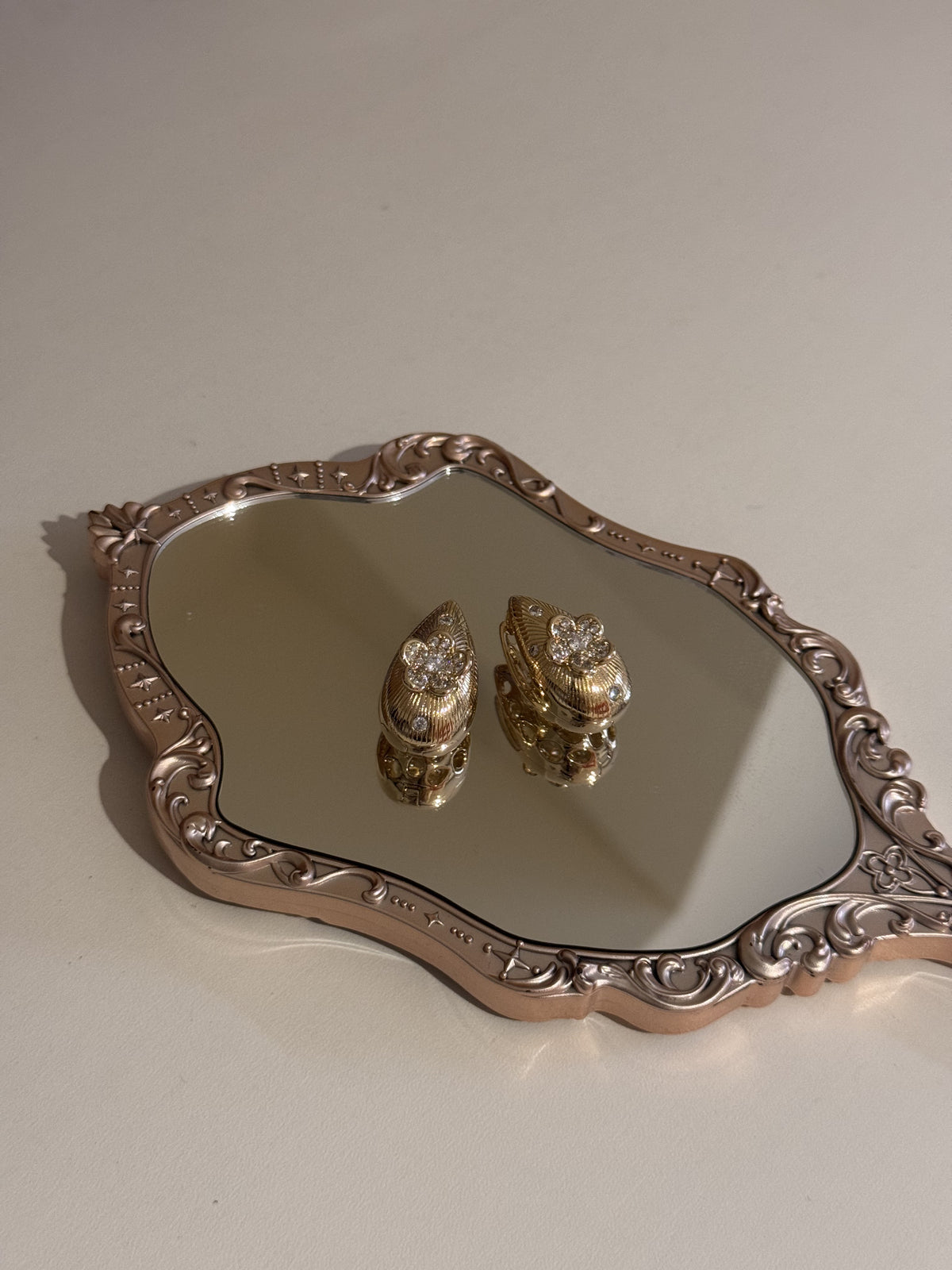 A pair of gold heart-shaped earrings with sparkling rhinestones displayed on a mirrored tray.