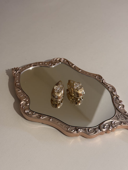 A pair of gold heart-shaped earrings with sparkling rhinestones displayed on a mirrored tray.