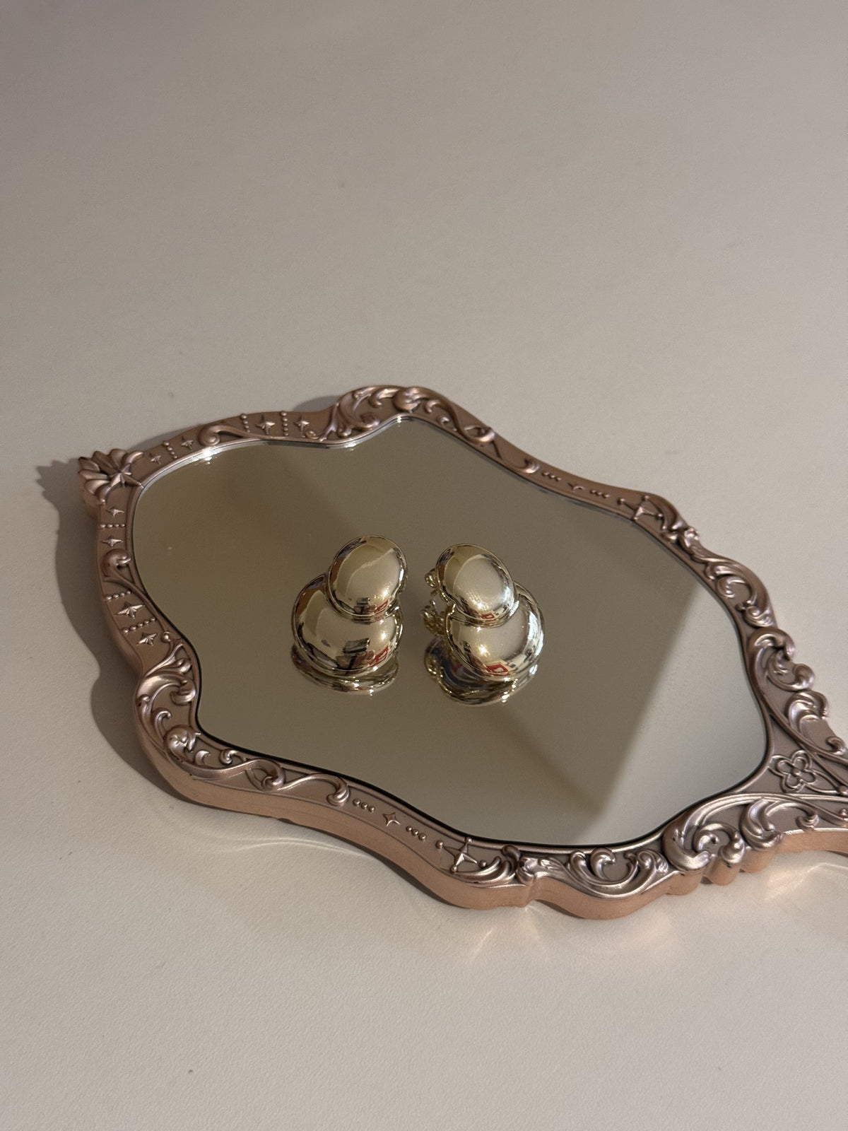 A pair of gold-tone oval earrings displayed on a mirrored tray.