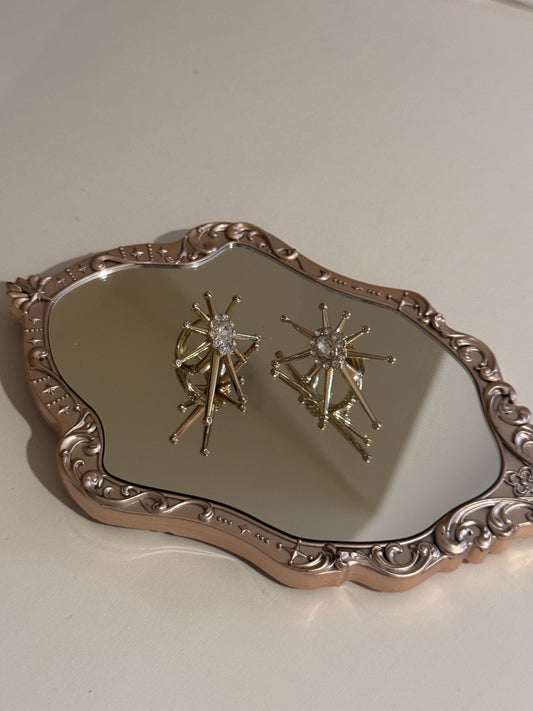A pair of gold-tone starburst earrings with clear crystal centers resting on a mirrored tray.