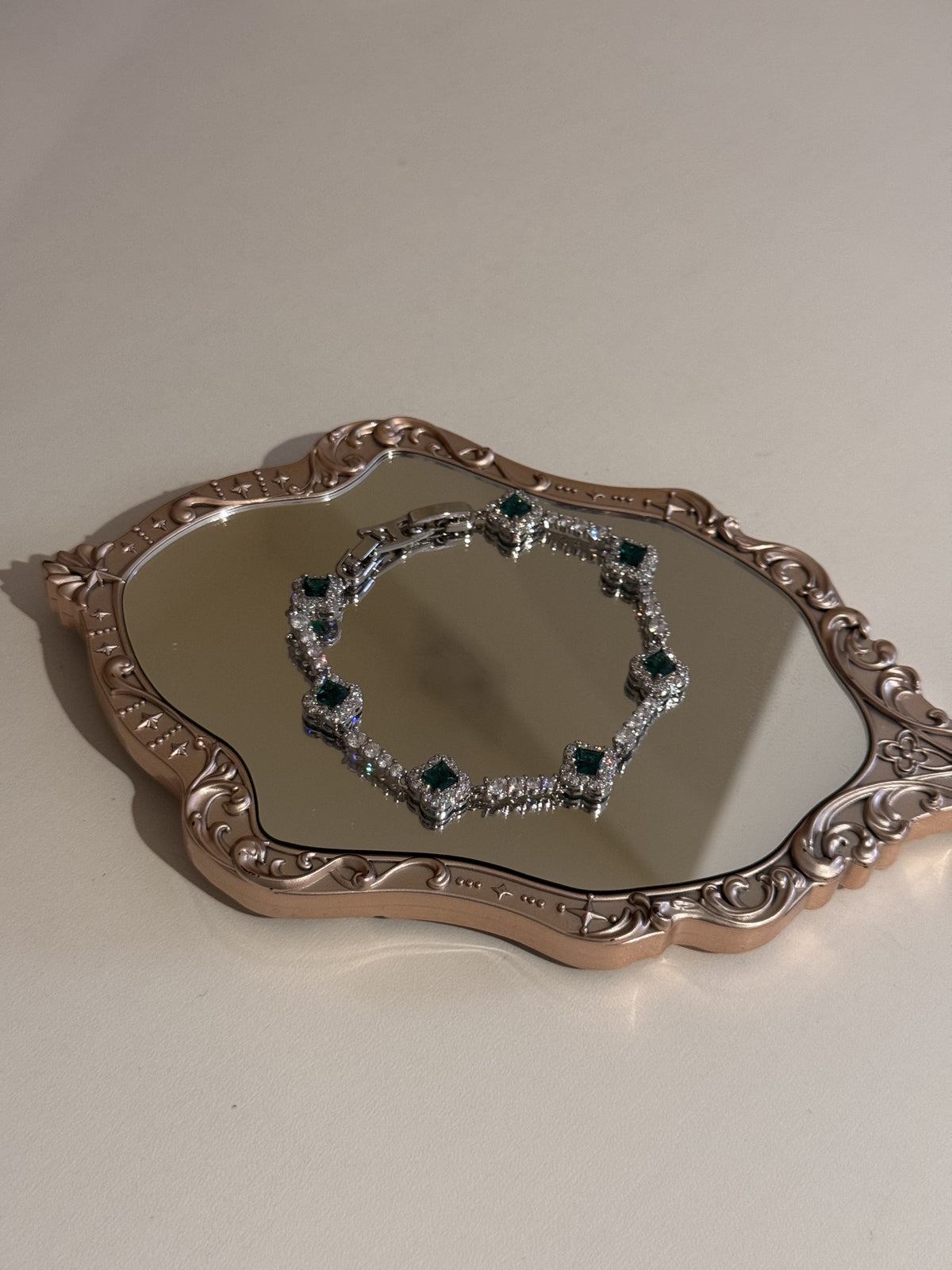 A silver-tone bracelet with square green stones and sparkling rhinestone accents resting on a mirrored tray.