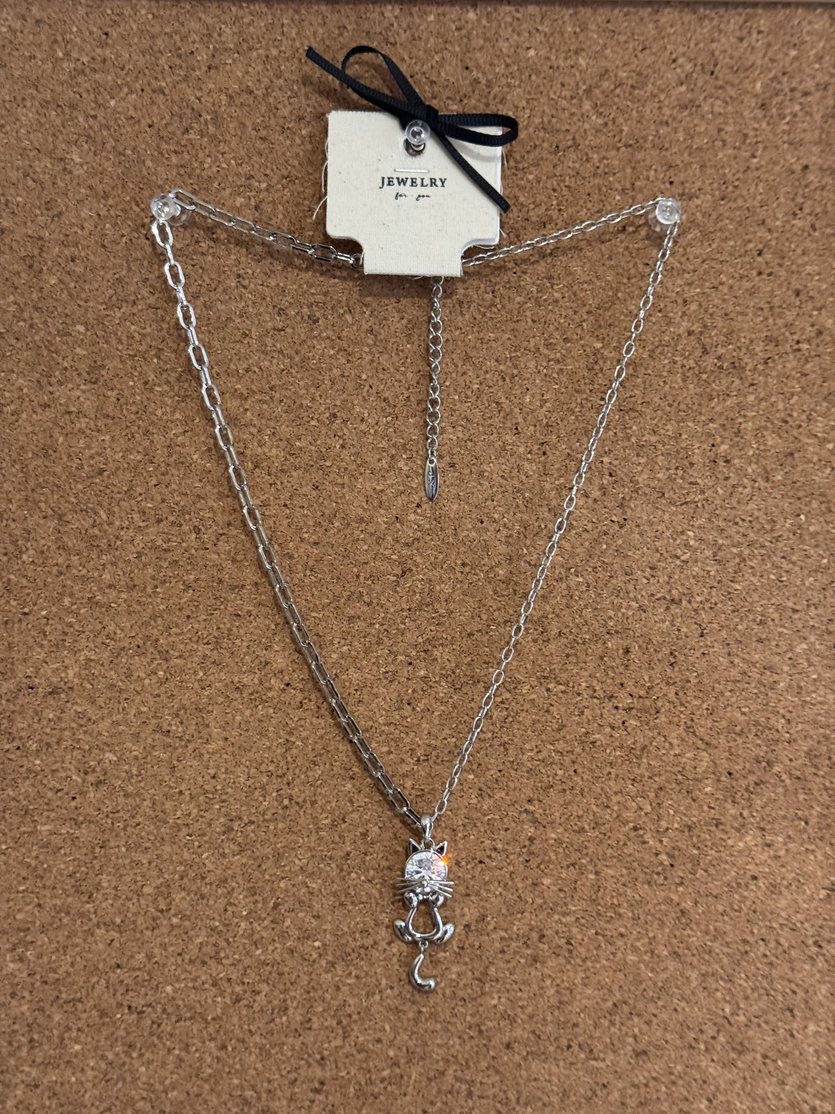 A silver-tone chain necklace featuring a small rhinestone-studded cat pendant with a curled tail.