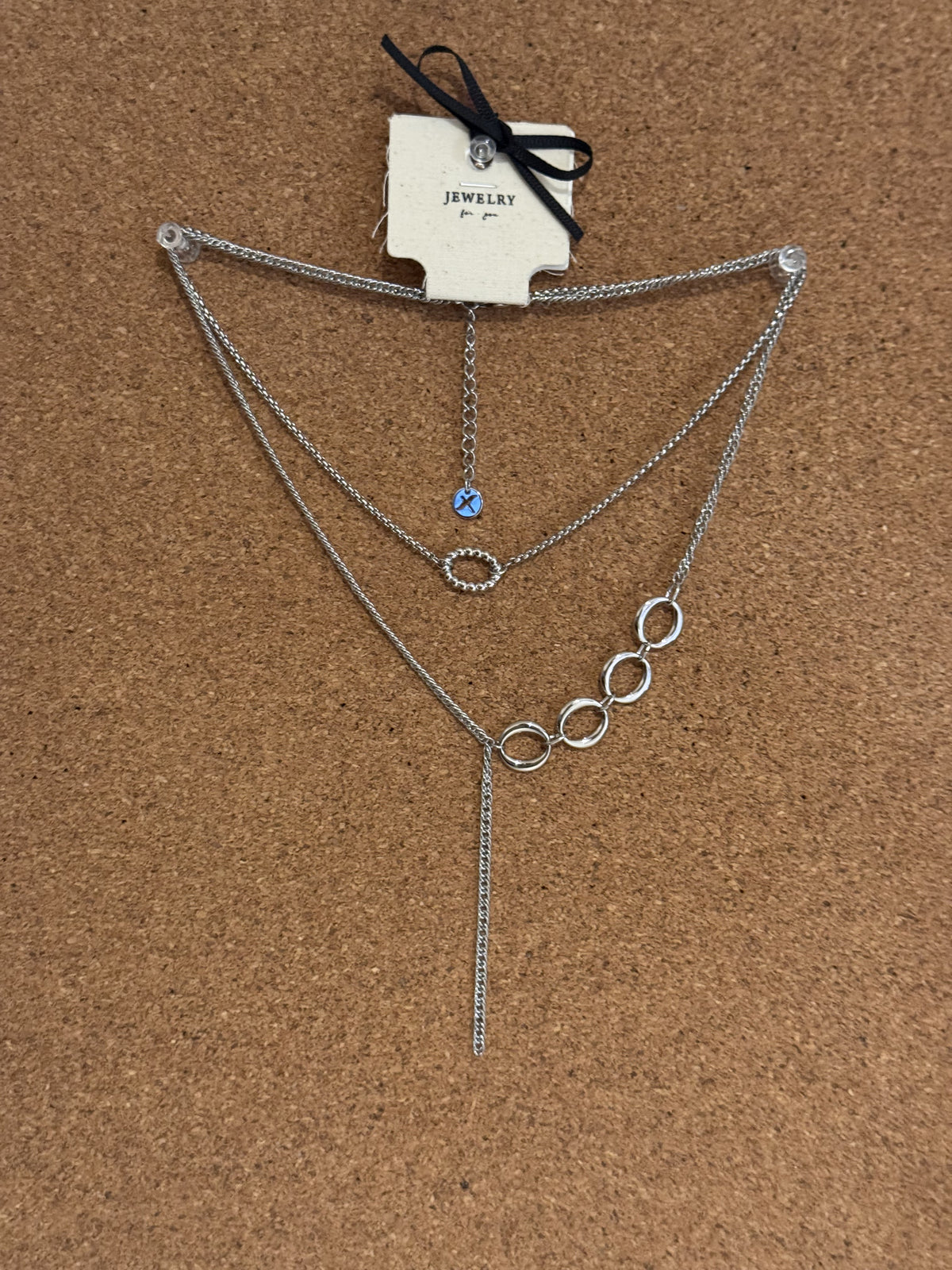 Silver-tone multi-layer necklace with interlocking circle links, a small blue bead charm and a dangling tassel chain.