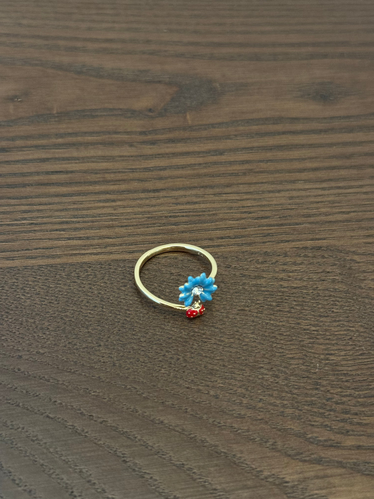 Gold-tone adjustable ring with a blue enamel flower charm and a tiny red bead dangle