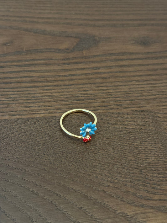 Gold-tone adjustable ring with a blue enamel flower charm and a tiny red bead dangle