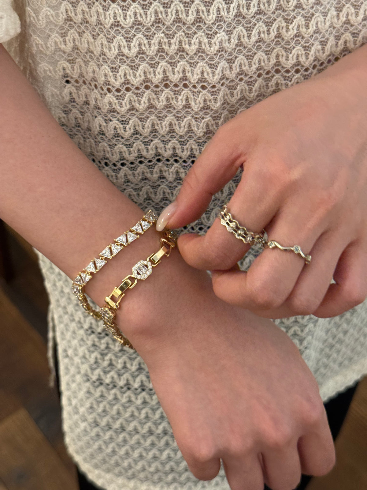 Close-up of layered gold bracelets and rings with clear stones on a woman's wrist, hand touching jewelry.