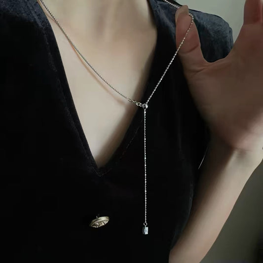 Silver Y-shaped lariat necklace with thin chain and small drop pendant on black V-neck top.