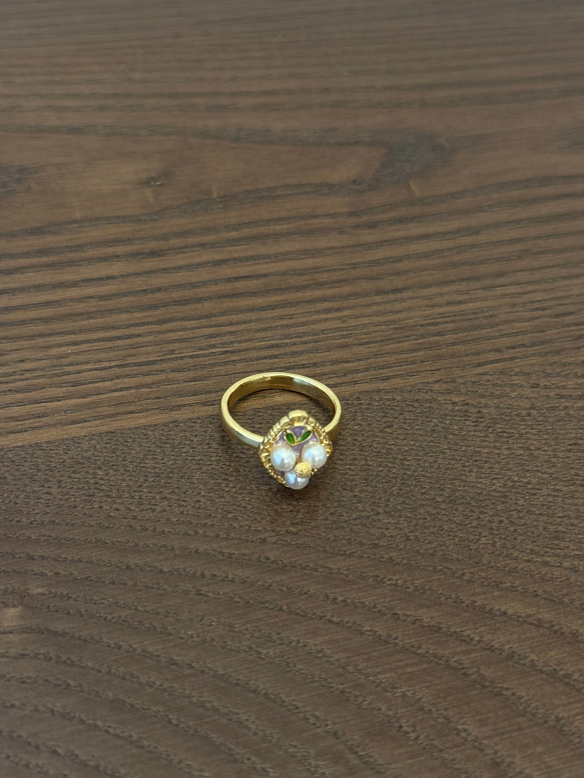 Gold-tone cluster ring with small white beads and a faceted clear center stone on wooden background.