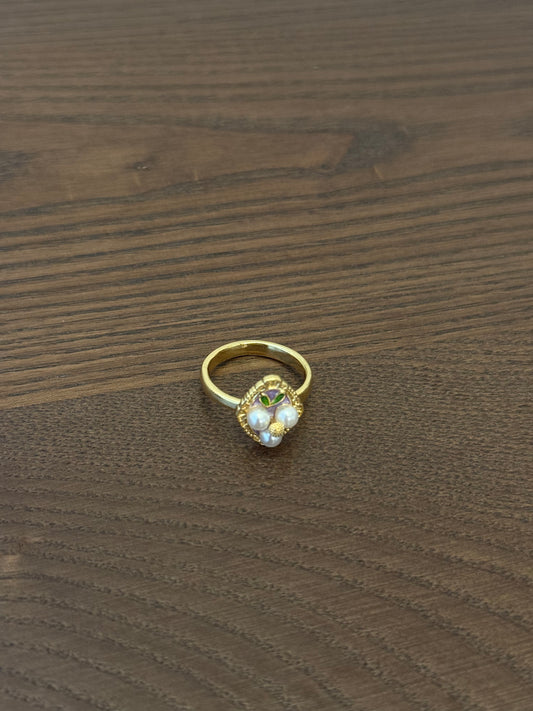 Gold-tone cluster ring with small white beads and a faceted clear center stone on wooden background.