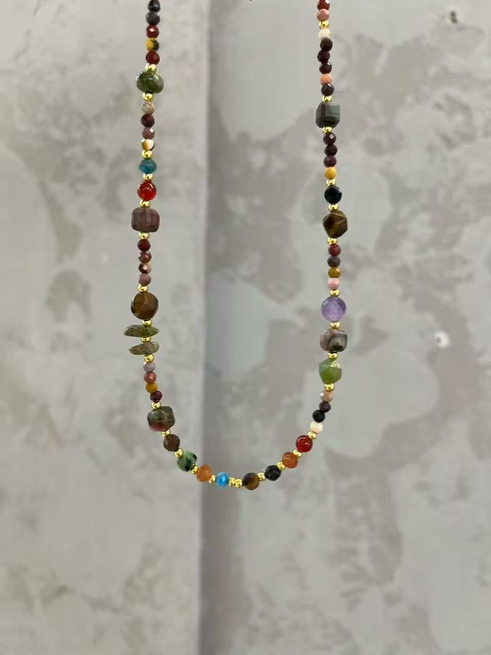 Colorful gemstone beaded necklace with gold spacers on a neutral background