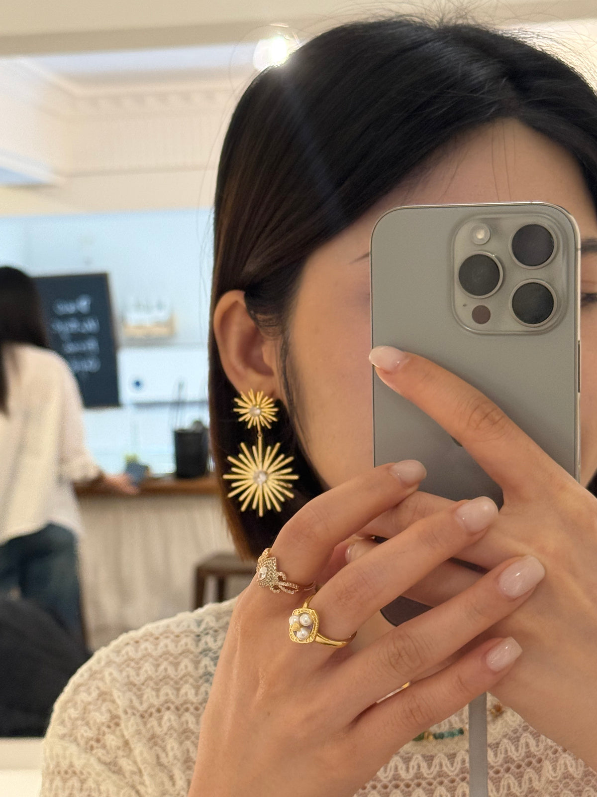 Woman wearing gold starburst earrings and pearl halo ring, elegant celestial fashion jewelry