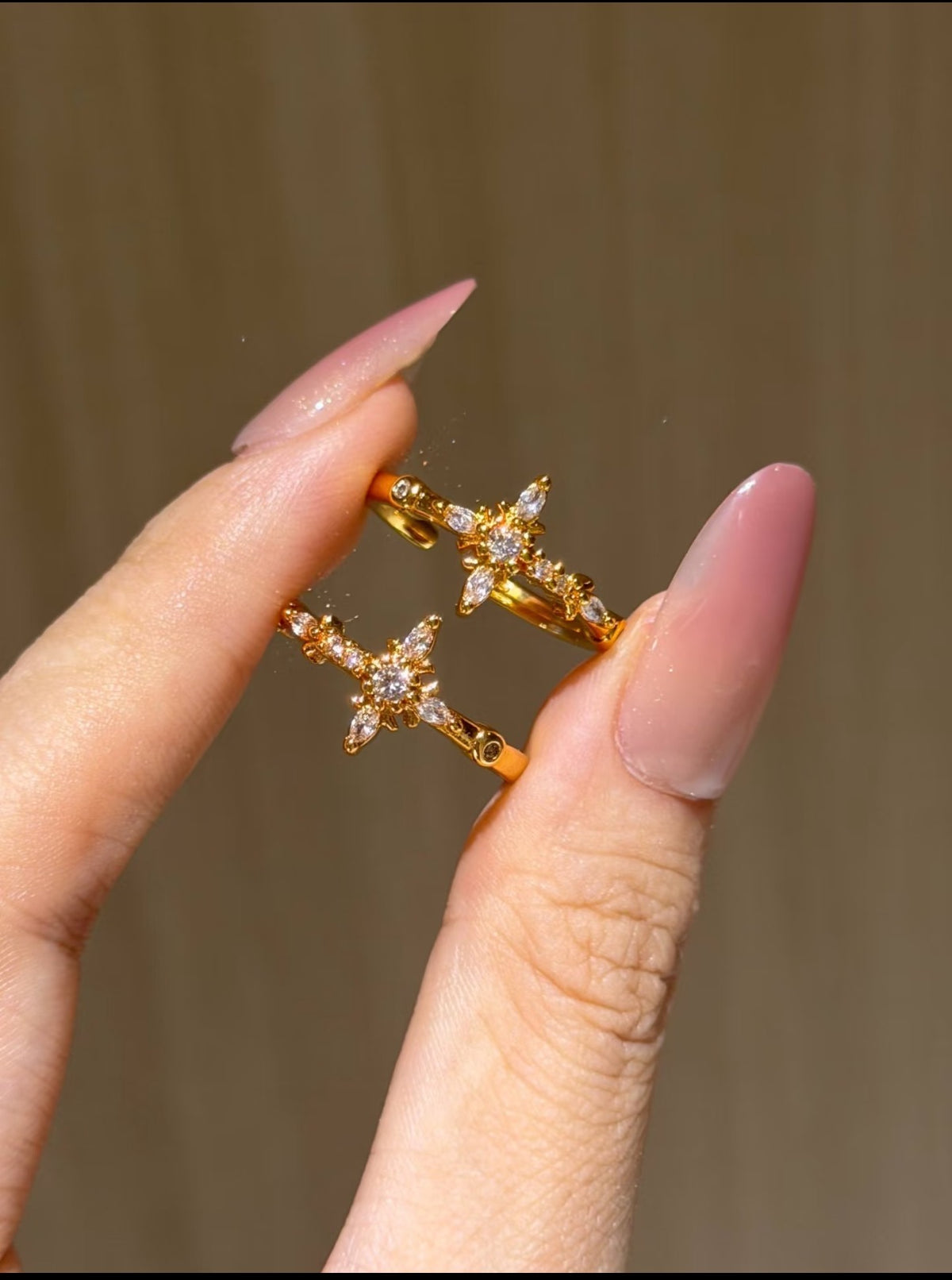 Hand holding two gold cross rings with clear crystal accents, dainty religious fashion jewelry close-up